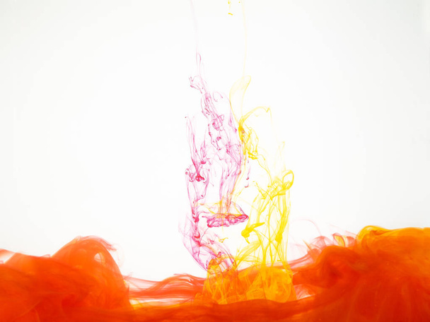 Abstract movement of yellow-red swirl under water. Yellow-red explosion of acrylic ink in water isolated on white background. Abstract colourful swirl background. Paint dissolving into water. - Φωτογραφία, εικόνα
