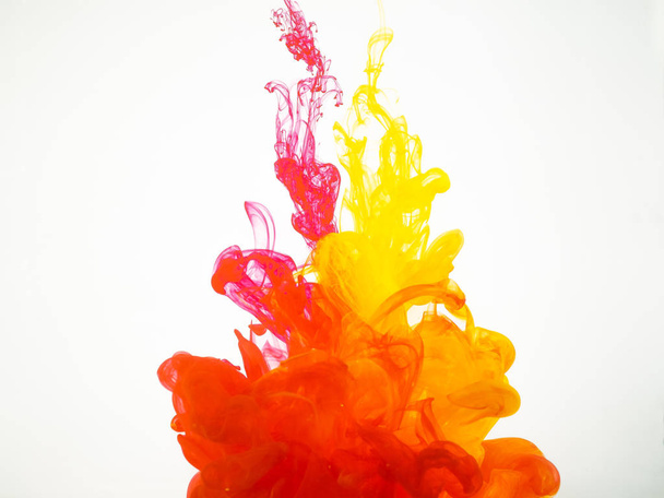 Movement of acrylic colours in water photographed while in motion. Abstract swirling of ink in water. Splash of ink isolated on white background. Yellow-red acrylic colour dissipation. - Foto, Bild