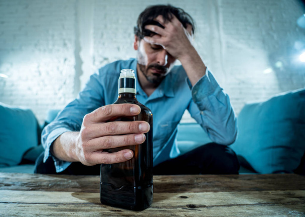 drunk alcoholic lain business man drinking whiskey from the bottle and glass depressed wasted and sad at home couch in alcohol abuse and alcoholism concept - Фото, изображение
