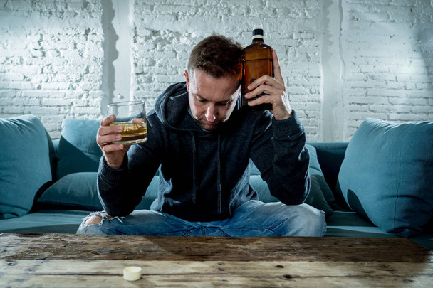 drunk alcoholic unemployed man drinking whiskey from the glass and bottle depressed wasted and sad at home couch in alcohol abuse and alcoholism concept - Foto, Imagen