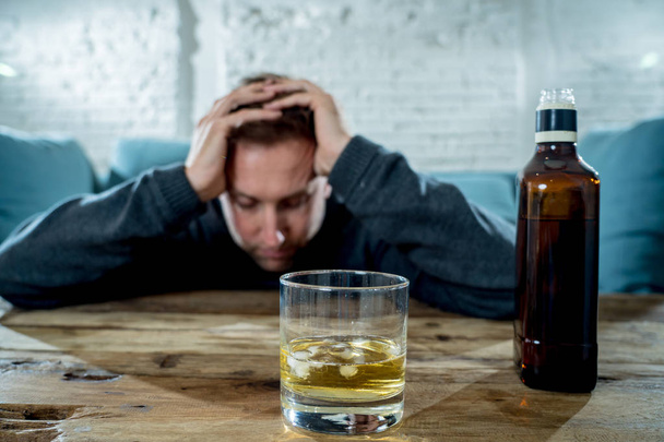 drunk alcoholic unemployed man drinking whiskey from the glass and bottle depressed wasted and sad at home couch in alcohol abuse and alcoholism concept - Fotografie, Obrázek