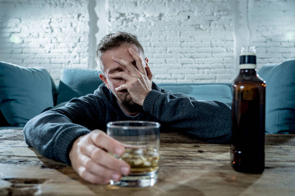 drunk alcoholic unemployed man drinking whiskey from the glass and bottle depressed wasted and sad at home couch in alcohol abuse and alcoholism concept - Фото, зображення