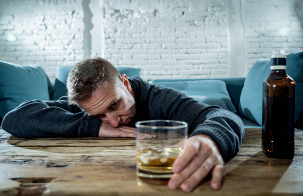 drunk alcoholic unemployed man drinking whiskey from the glass and bottle depressed wasted and sad at home couch in alcohol abuse and alcoholism concept - Valokuva, kuva