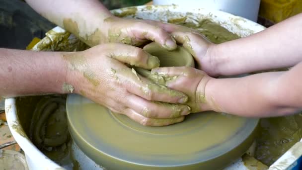De Potters handen hebben de vorm van een kopje uit een klei. Het proces van het creëren van aardewerk op een potter van wiel. De master keramist leert de leerling om een pot in zijn atelier. Close-up, alleen handen. - Video