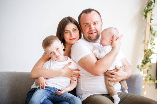 Portrait of happy young parents with two sons sitting on sofa - Fotografie, Obrázek