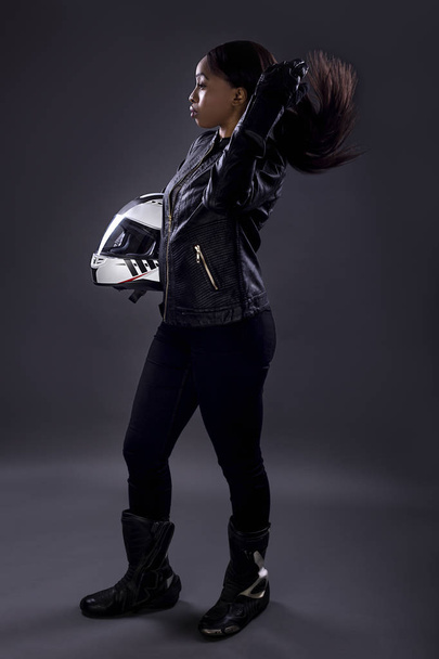 Motociclista nero femminile o pilota di auto da corsa o stuntwoman indossando tuta da corsa in pelle e tenendo un casco protettivo. Lei è in piedi con fiducia in uno studio
 - Foto, immagini
