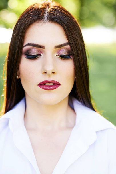 Roztomilá mladá brunetka s krásným profesionální make-up na zeleném pozadí v parku. - Fotografie, Obrázek