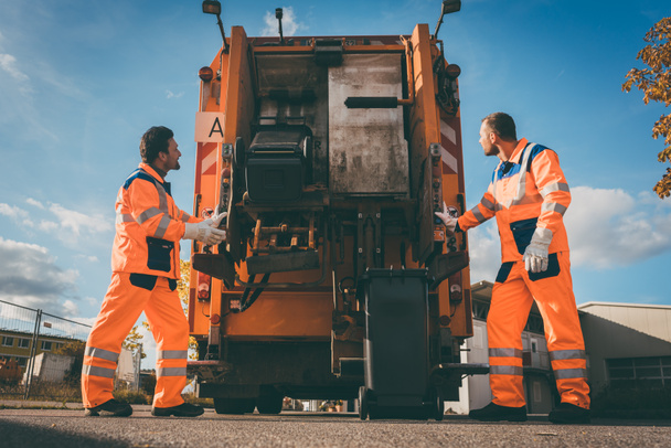 Zwei Mitarbeiter der Müllabfuhr laden Müll in Müllwagen - Foto, Bild