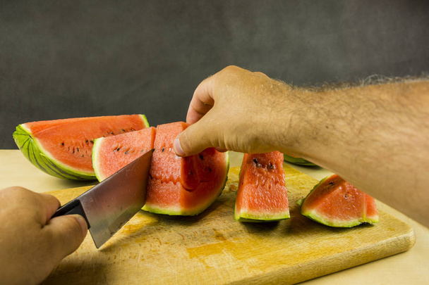 Cuchillo de cortar la sandía jugosa roja madura en una tabla de cortar
. - Foto, Imagen