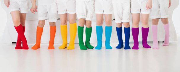 カラフルな虹の靴下を着ている子供たち。子供靴コレクション。ニット膝の高い靴下やタイツの様々な。子供服やアパレル。子供のファッション。足と足の小さな男の子と女の子のグループ. - 写真・画像