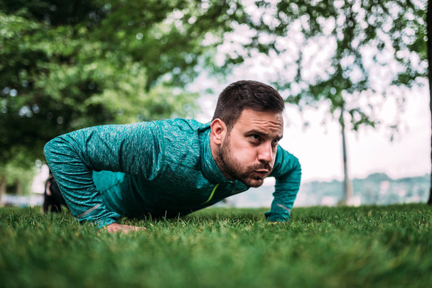 Close-up image of man doing push-ups outdoors. Making a face. - Foto, afbeelding