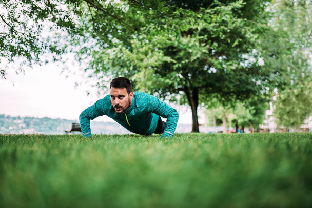 Committed young man doing push-ups on the grass. - Foto, afbeelding
