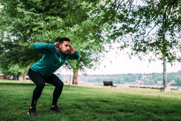 Full length of young concentrated sportsman doing squats outdoors. - Foto, Bild