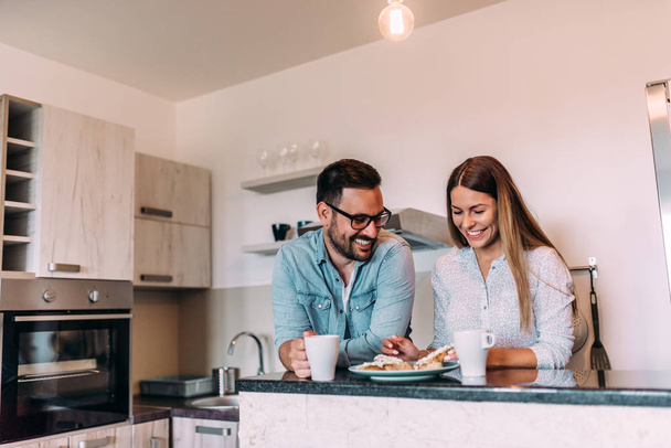 Cute couple eating breakfast in the kitchen and having a good time. - Foto, imagen