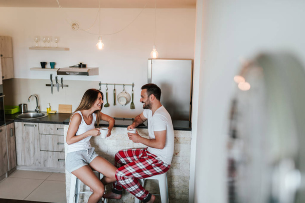 Couple in pajamas drinking tea or coffee at the kitchen counter. - Foto, imagen