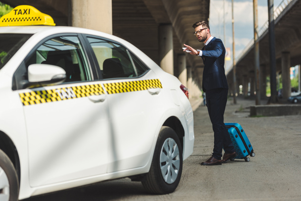 stylish young man with smartphone and suitcase looking at taxi cab - Foto, imagen