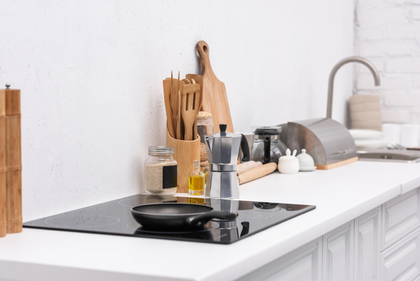 koekenpan op inductie paneel op moderne keuken met diverse gebruiksvoorwerpen - Foto, afbeelding