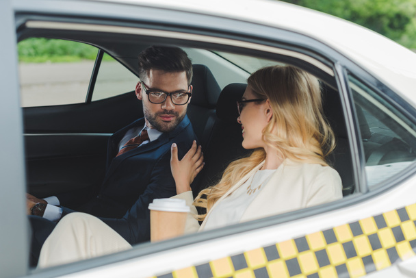 smiling young woman holding paper cup and flirting with handsome man sitting in taxi - Photo, Image