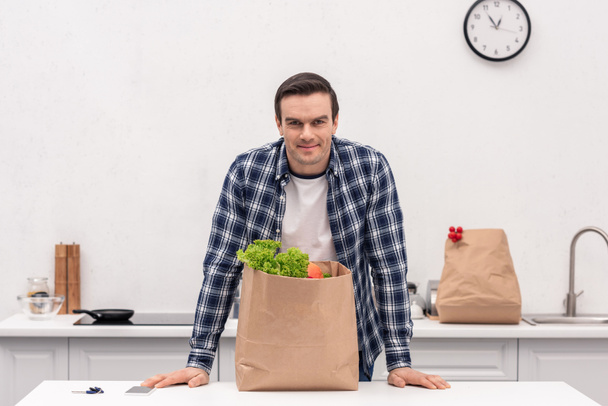 handsome adult man with grocery store paper bag at kitchen - Fotó, kép
