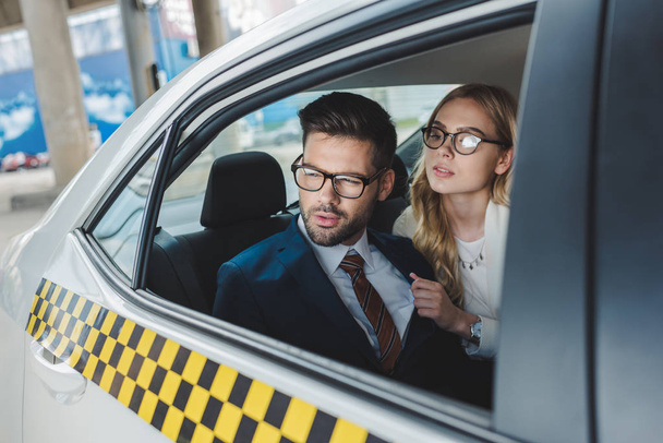 stylish young couple in formal wear and eyeglasses looking away while sitting together in taxi - Photo, Image