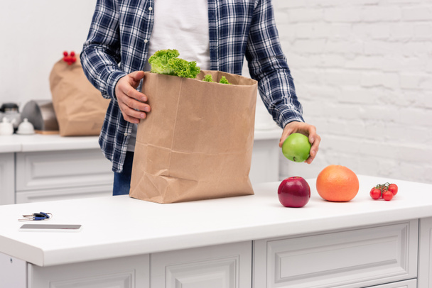 cropped shot of man unpacking grocery store paper bag at kitchen - Foto, afbeelding