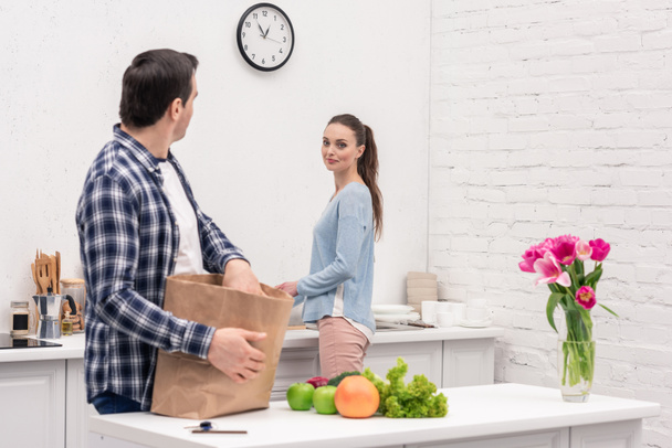 adult man chatting with wife while unpacking bag from grocery store - Photo, Image