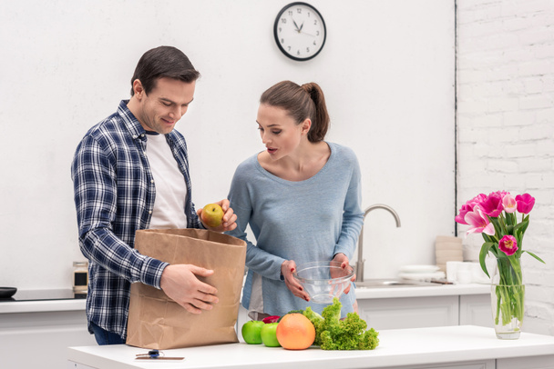 surprised adult couple unpacking paper bag after grocery shopping - Foto, Bild