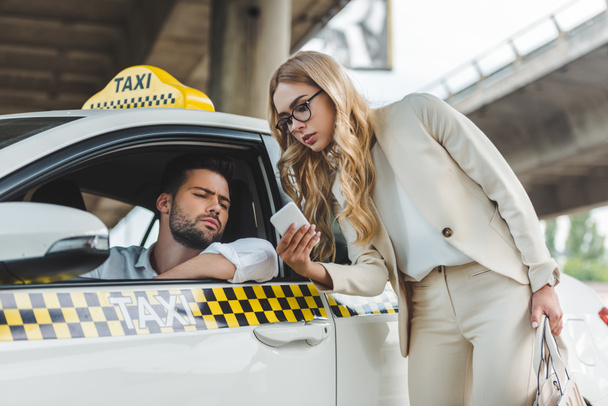 stylish blonde woman showing smartphone to the taxi driver - Zdjęcie, obraz