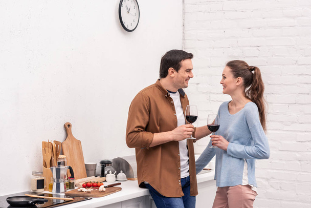 beautiful adult couple with glasses of wine spending time together at kitchen - Photo, Image