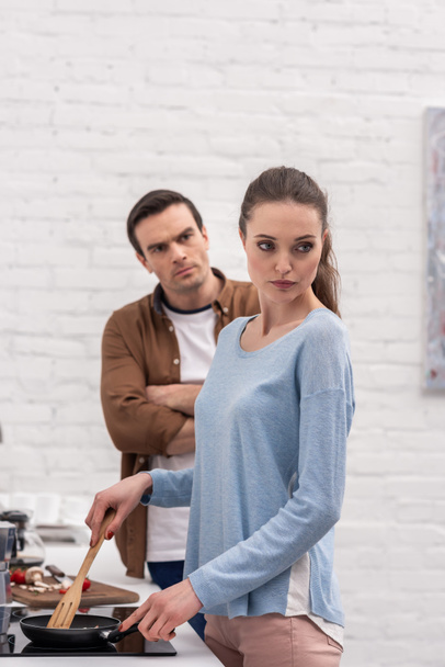 θυμωμένος ενηλίκων άνδρας ψάχνει γυναίκα ενώ η ίδια αγνοώντας τον μετά το όρισμα στην κουζίνα - Φωτογραφία, εικόνα