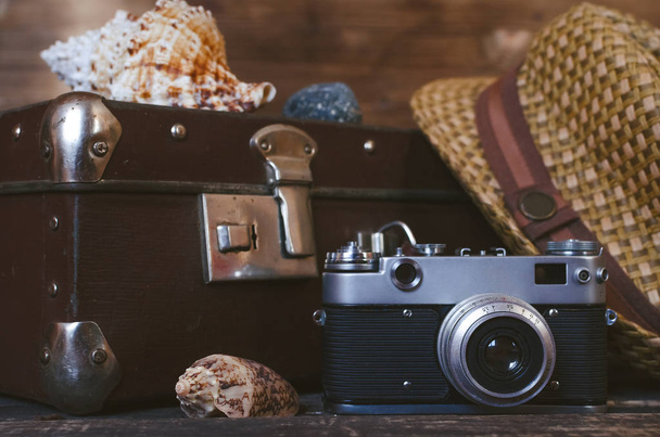 Retro summer sea vacation background. Vintage suitcase, film camera, hat and seashells on tourist table. Front view, close up photo. - Foto, Bild