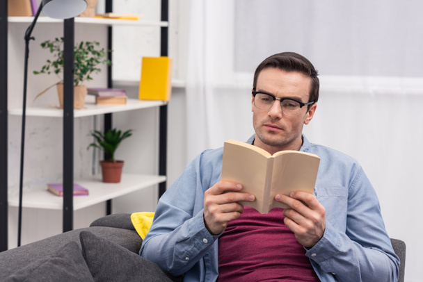 concentrated adult man reading book on couch at home - Foto, Imagen