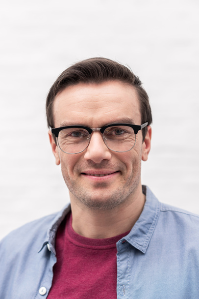 close-up portrait of smiling adult man in eyeglasses looking at camera in front of white wall - Photo, Image