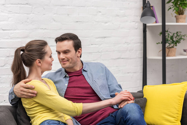 happy adult couple holding hands while sitting on couch at home - Photo, Image