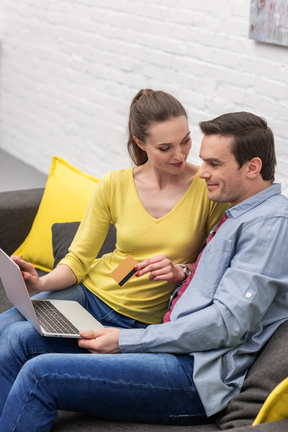 smiling adult couple making e-shopping with laptop and credit card on couch at home - Photo, Image