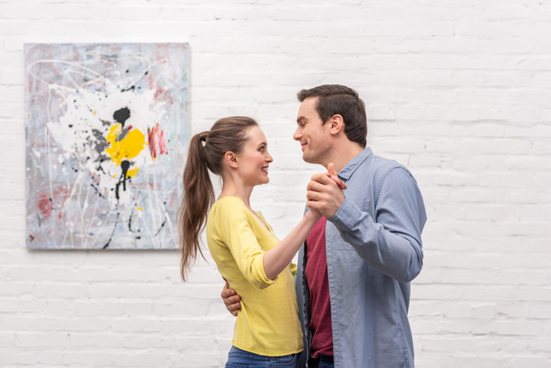 happy adult couple dancing in front of white brick wall with abstract picture - Fotó, kép