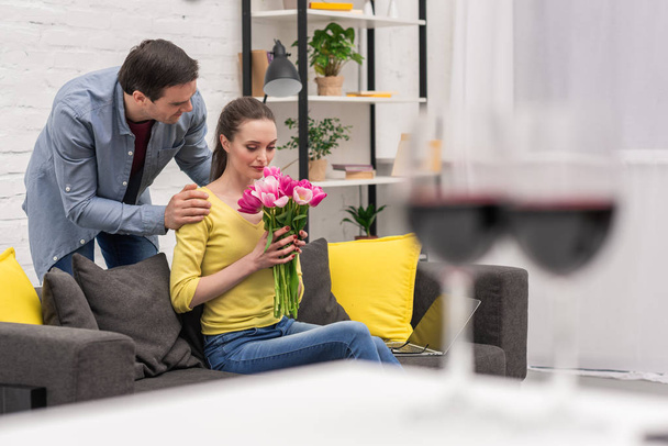 guapo adulto hombre presentando ramo de tulipanes a esposa en casa
 - Foto, Imagen