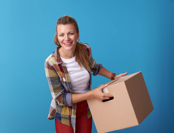 smiling active woman in white shirt holding a cardboard box on blue background - Zdjęcie, obraz