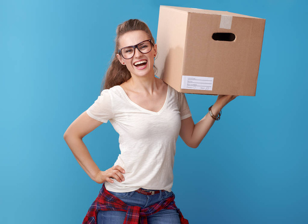 Portrait of smiling young woman in white shirt with a cardboard box on blue background - Fotoğraf, Görsel