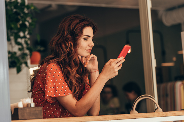 a fiatal nő használ smartphone kávézóban oldalnézete - Fotó, kép