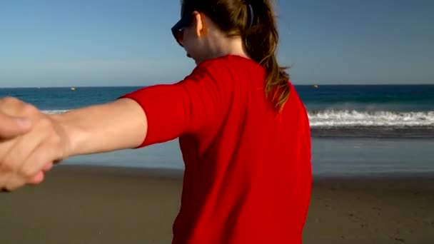Suivez-moi - heureuse jeune femme en robe rouge tirant les gars main. Main dans la main marchant vers l'eau sur la plage de l'océan au coucher du soleil. Mouvement lent
 - Séquence, vidéo