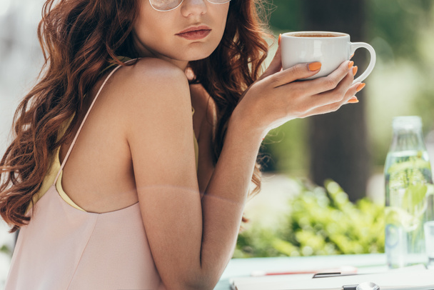 vista parcial de la mujer sosteniendo la taza de café en las manos en la cafetería
 - Foto, Imagen