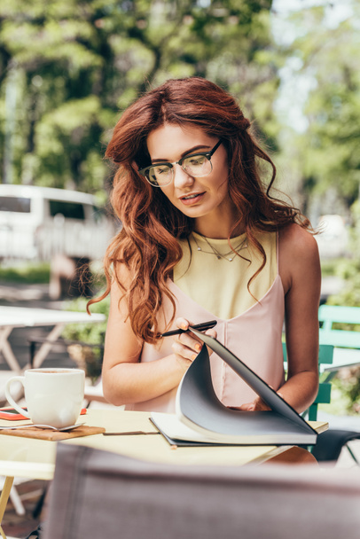 portrait of young businesswoman in eyeglasses with notebook at table in cafe - Photo, Image
