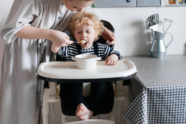 a caring good mother feeds her young son with a delicious soup in the kitchen, a family dinner - Valokuva, kuva