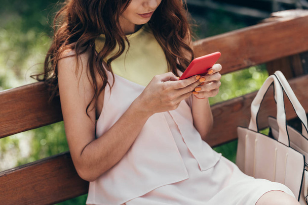 partial view of stylish woman using smartphone while resting on bench - Foto, afbeelding