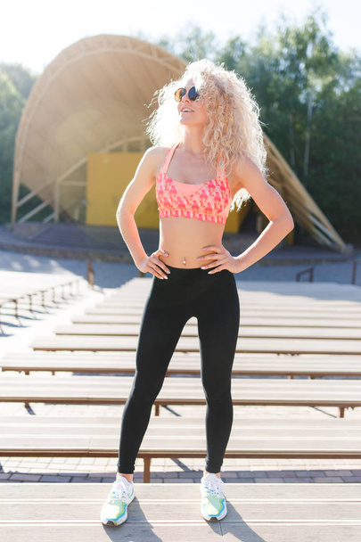 Photo of curly-haired athletic woman standing in park among shops - Photo, image