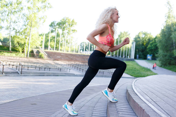 Photo of curly-haired athletic woman running through park among benches - Photo, image