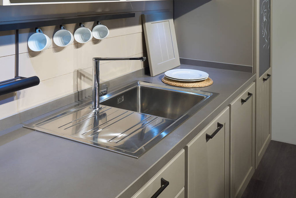 Сучасні кухонні меблі, нержавіюча мийка, металевий міксер і деякі білі керамічні посуд
 - Фото, зображення