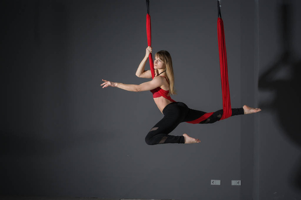 Fly yoga. Young woman practices aerial anti-gravity yoga with a hammock in fitness club on gray background. - Fotó, kép