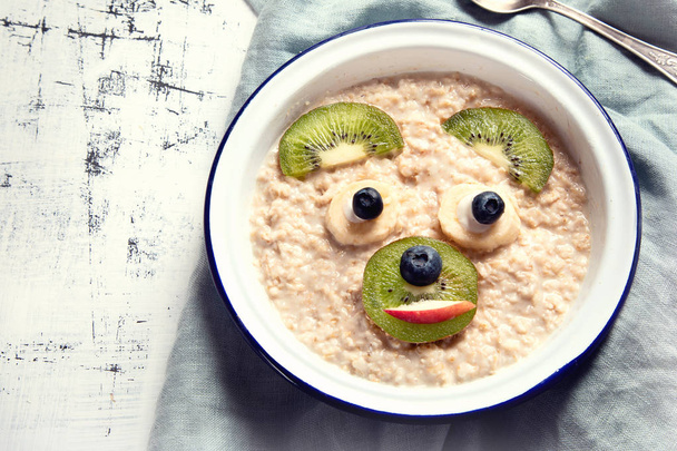 Bowl of oatmeal porridge with fruits breakfast for kids on kitchen table - Valokuva, kuva